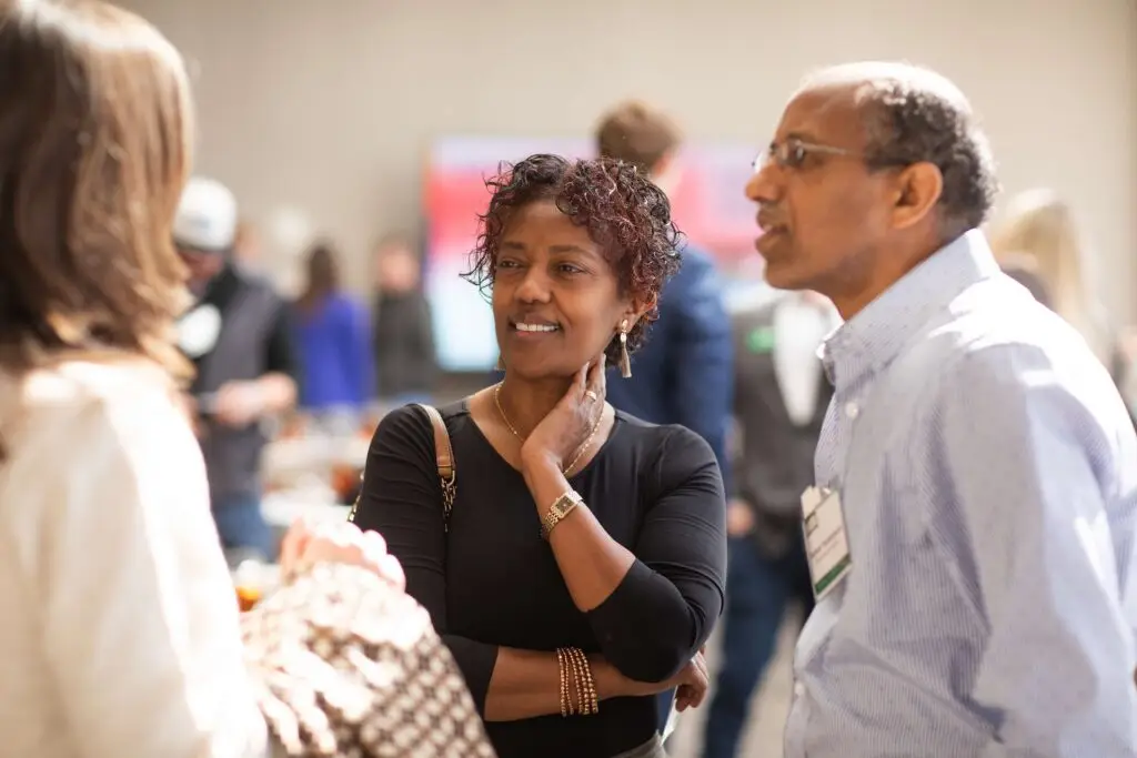 Conference attendees listening and talking during a networking session in a bright event space.