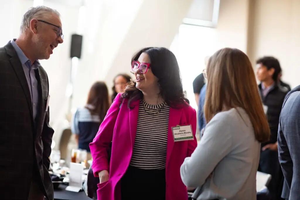 Three professionals talking and smiling during a networking session at a business conference.