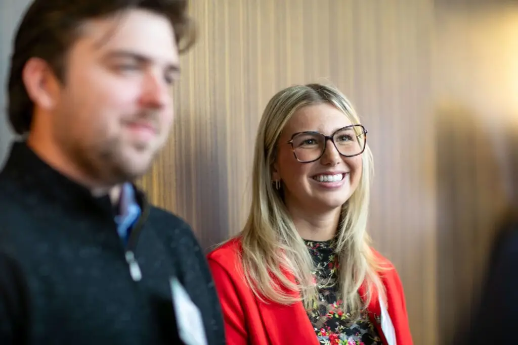 Smiling conference attendee in a red blazer listening during a networking event.